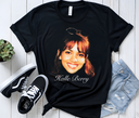 "Flat lay composition: Black vintage Halle Berry 90s supermodel graphic tee arranged on white wooden surface with faded blue jeans and classic black sneakers, creating retro streetwear outfit inspiration"